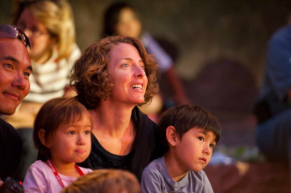 Two adults and two children listening to a story. There are people behind them in a blurred image.