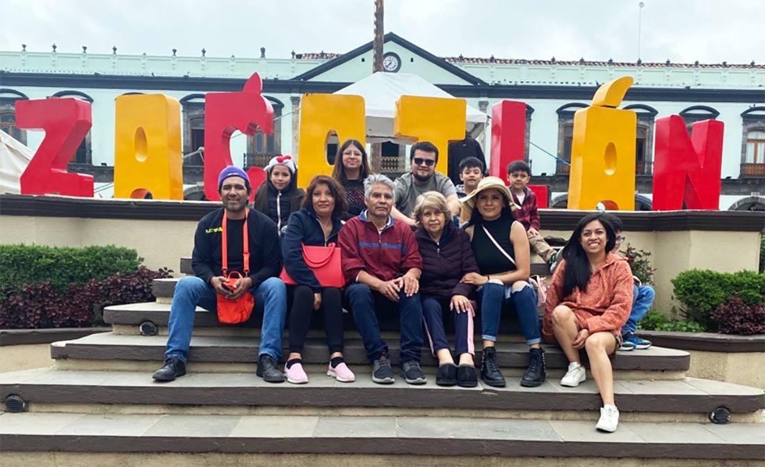A Mexican family sits on steps in front of a sign that says Zacotlan