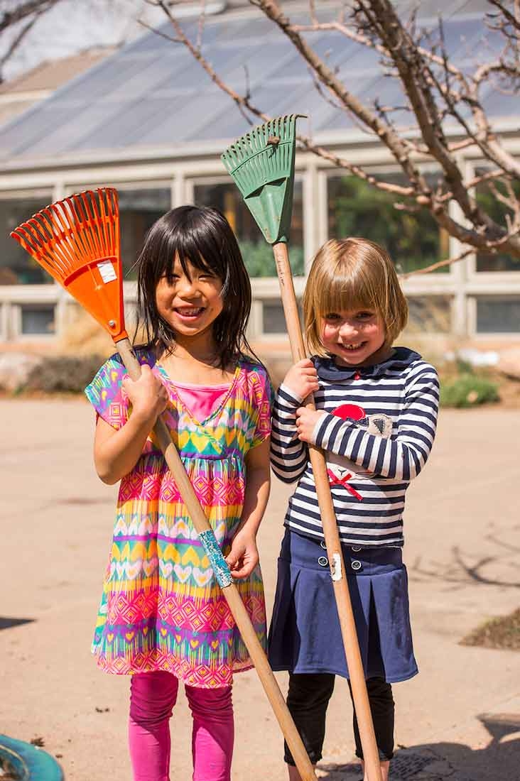 Two children holding gardening tools while outside.