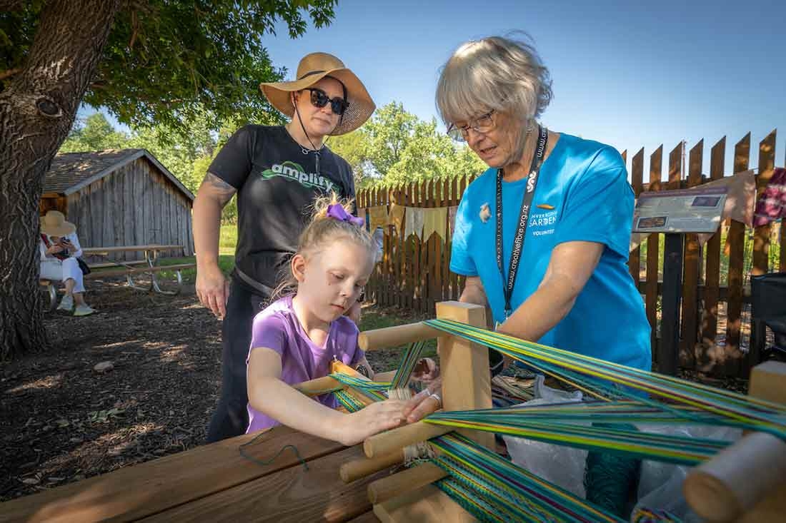 Two adults and one child weaving at Lavender Festival