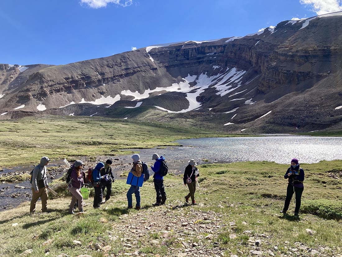 A group of people with a body of water and mountain behind them