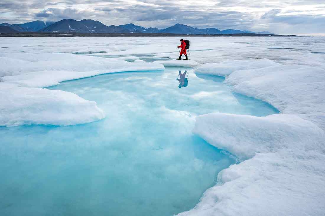 An archaeologist treks past an open melt pool on the sea ice between Inuit Qeqertaat (Kaffeklubben Island) and the mainland. 
