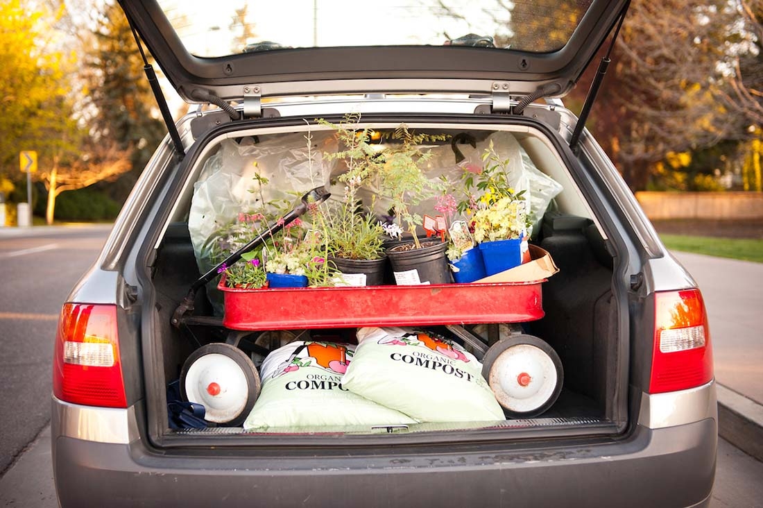 Open car hatch stuffed with red wagon holding lots of plants