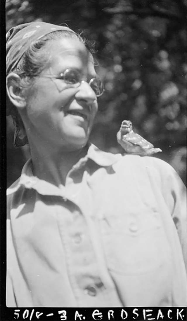 black and white image of woman in glasses smiling at bird on her shoulder