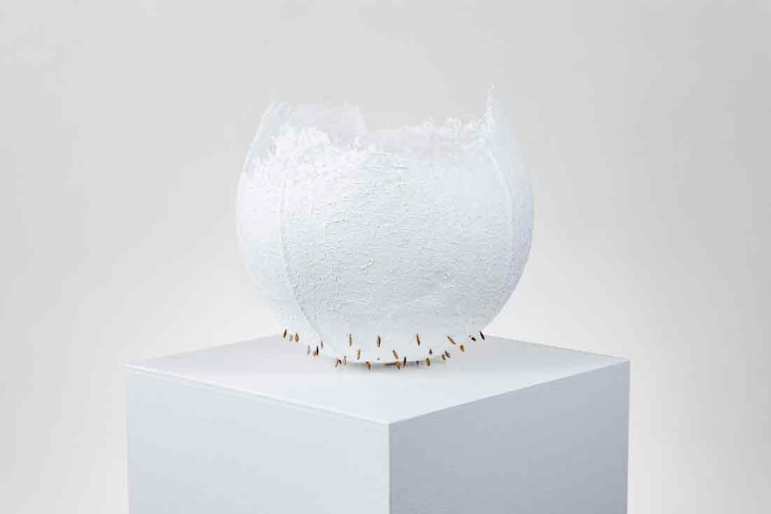 White sculpture with wheat spikes and gold paint sitting on a white pedestal.