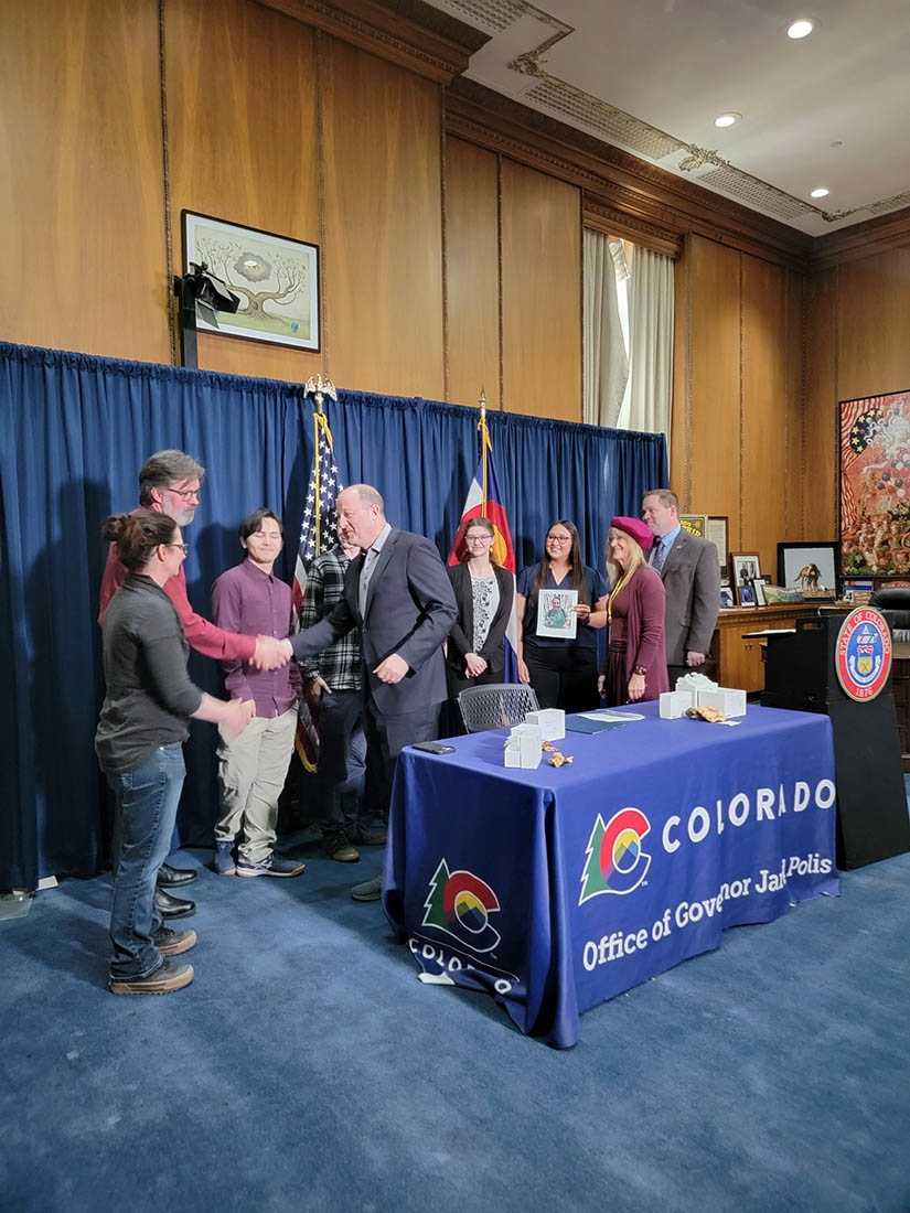 Andy Wilson shakes hands with Governor Polis