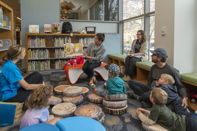 Woman reading from picture book to group of children and adults